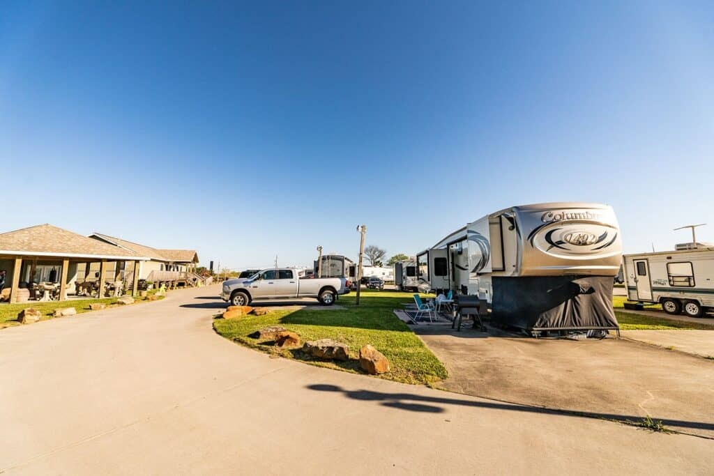 Concrete paved resort street with fifth-wheels and travel trailers on full-hookup sites — Gulf Coast 5 Star RV Resort, Oyster Creek TX